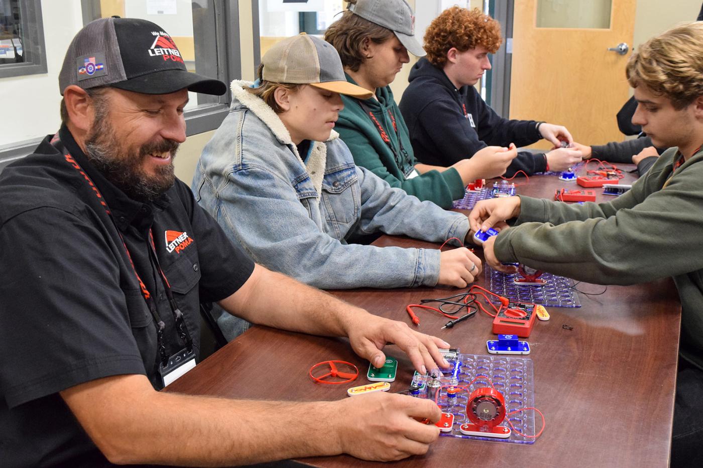A Leitner-Poma instructor works alongside students as they build and test simple electrical circuits during a hands-on classroom session for The Pipeline Project, introducing students to technical skills used in the mountain resort industry.